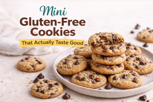 Mini gluten-free chocolate chip cookies on a plate with one cookie broken open to show a chewy center